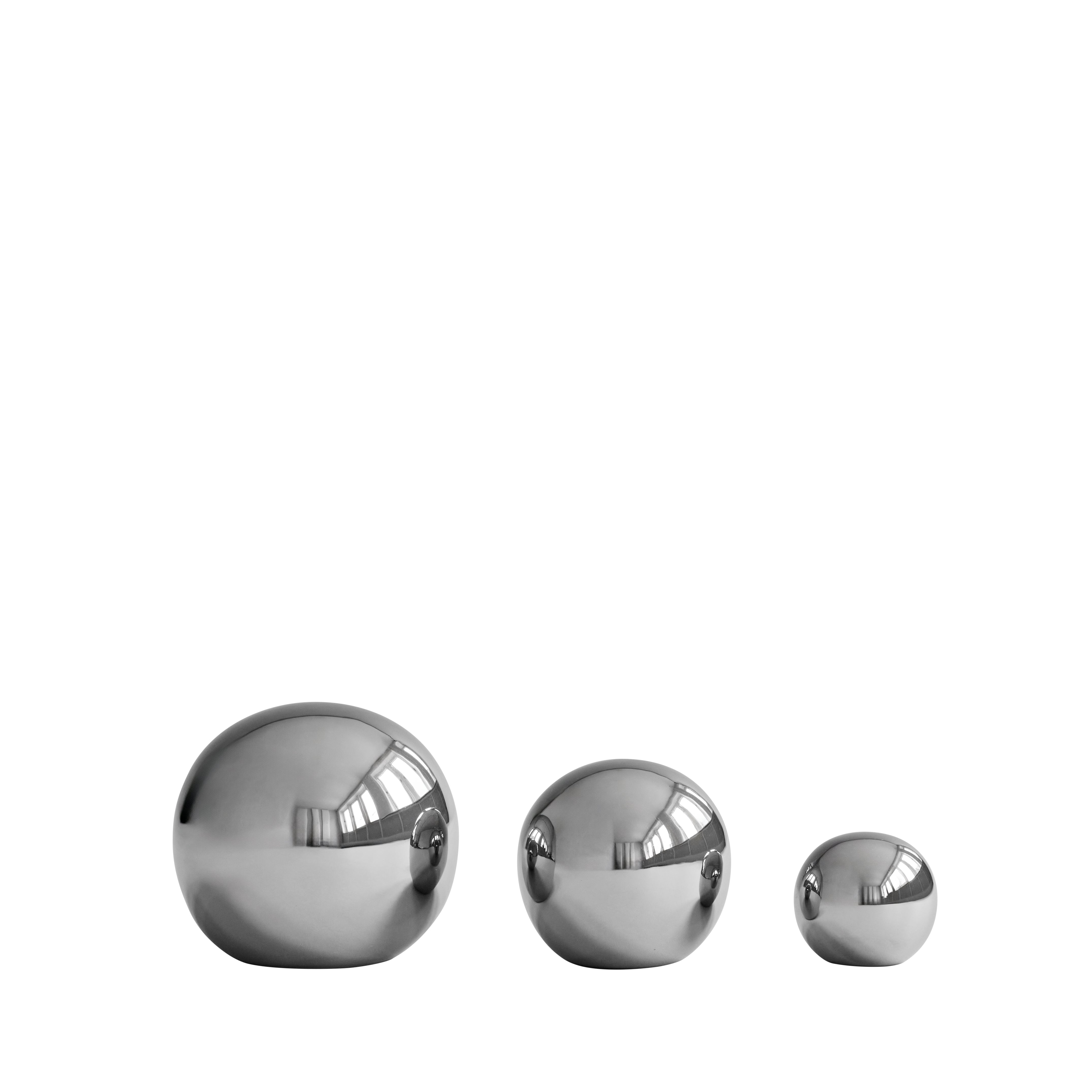 Three reflective chrome spheres of varying sizes against a White background. The polished surfaces reflect a minimalist studio setting