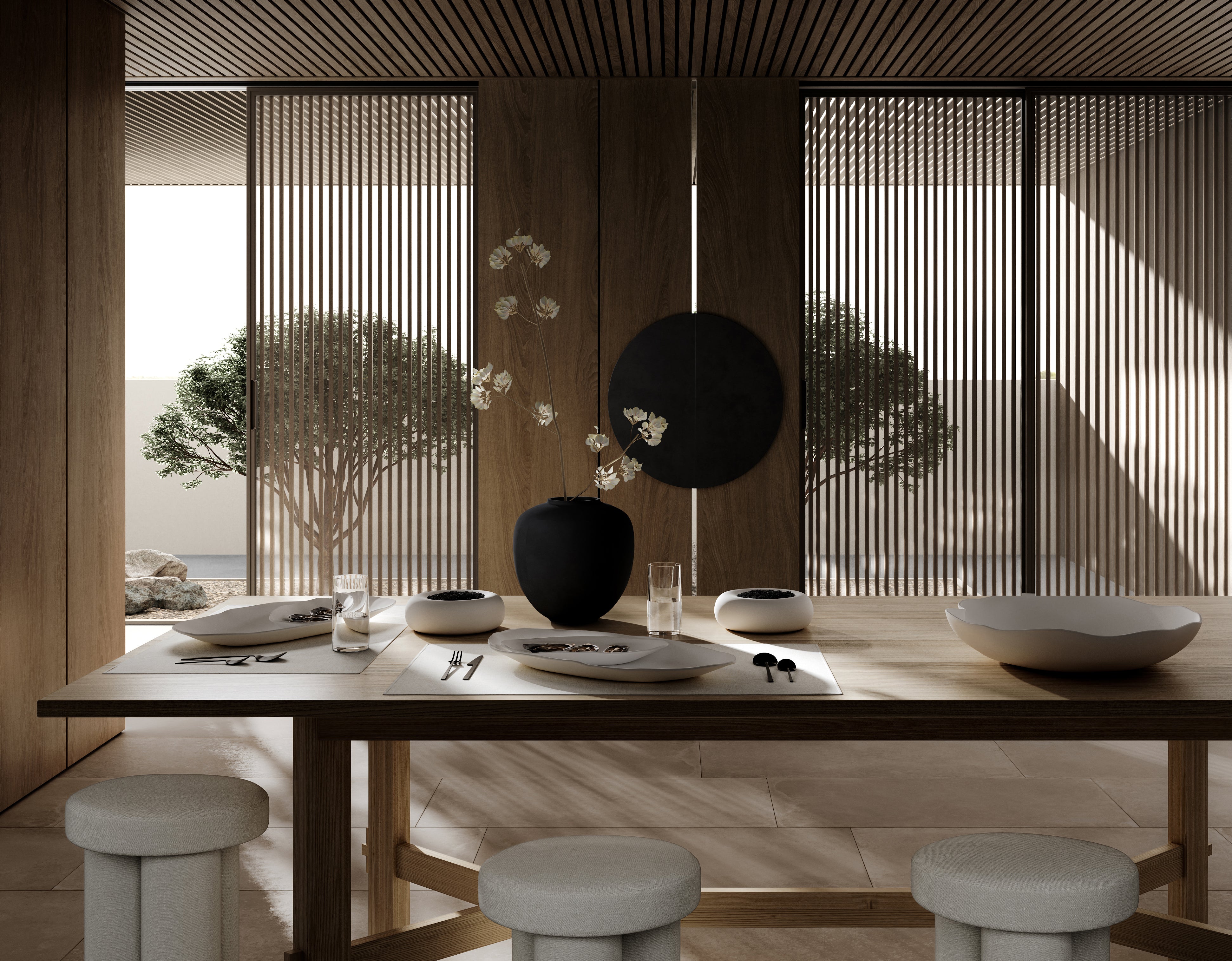 Elegant dining space featuring a wooden table set with ceramic tableware and black decorative accents. Behind the table, four Big Foot Stools upholstered in a soft neutral fabric are arranged. Large wooden screens and slatted panels allow sunlight to filter in, casting dynamic shadows. A tree is visible outside the window, adding a natural element to the modern interior.